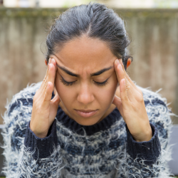 woman holding her hands to the side of her head, grimacing and rubbing temples